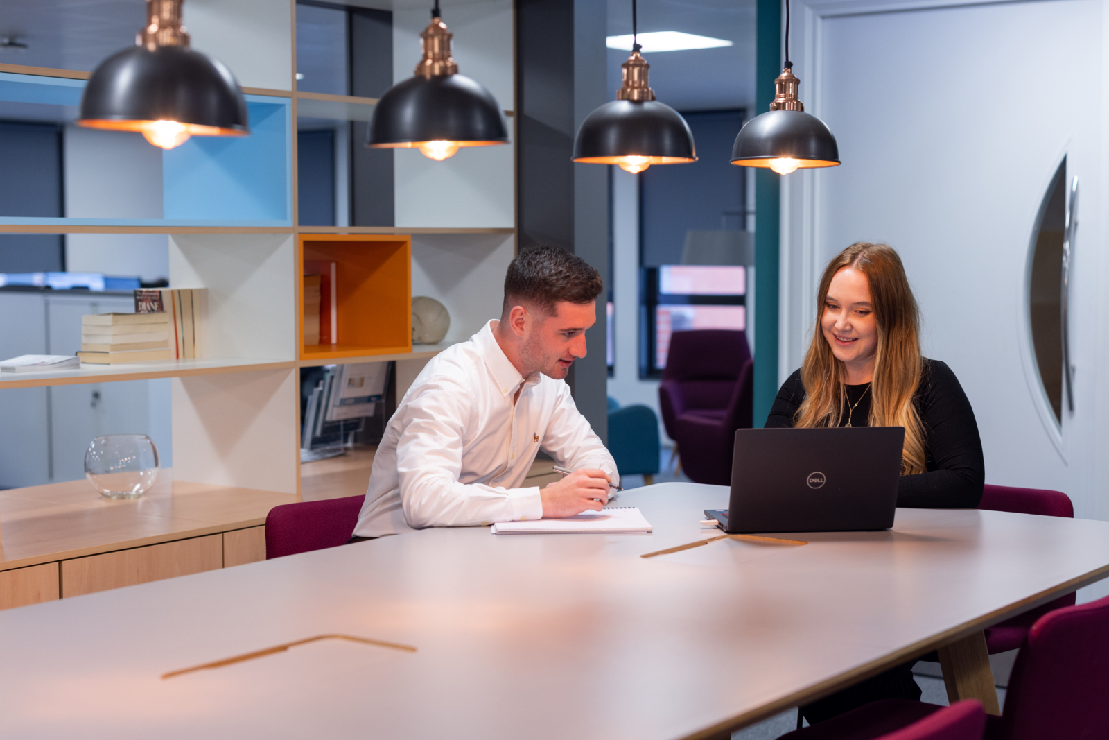 A man and woman sitting at a table in an office working together