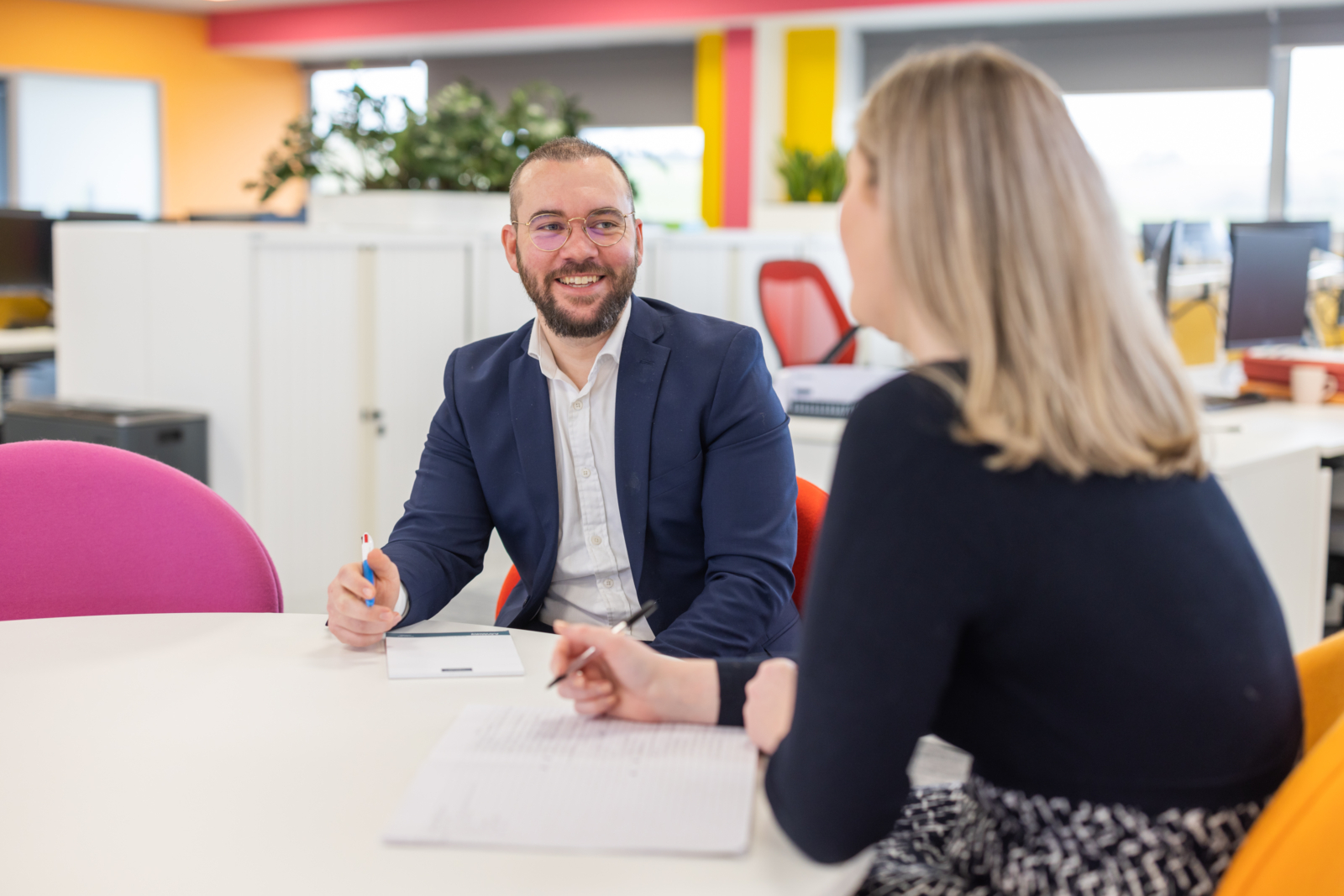 two people sitting at a table wearing business clothes. There is a a man and a women