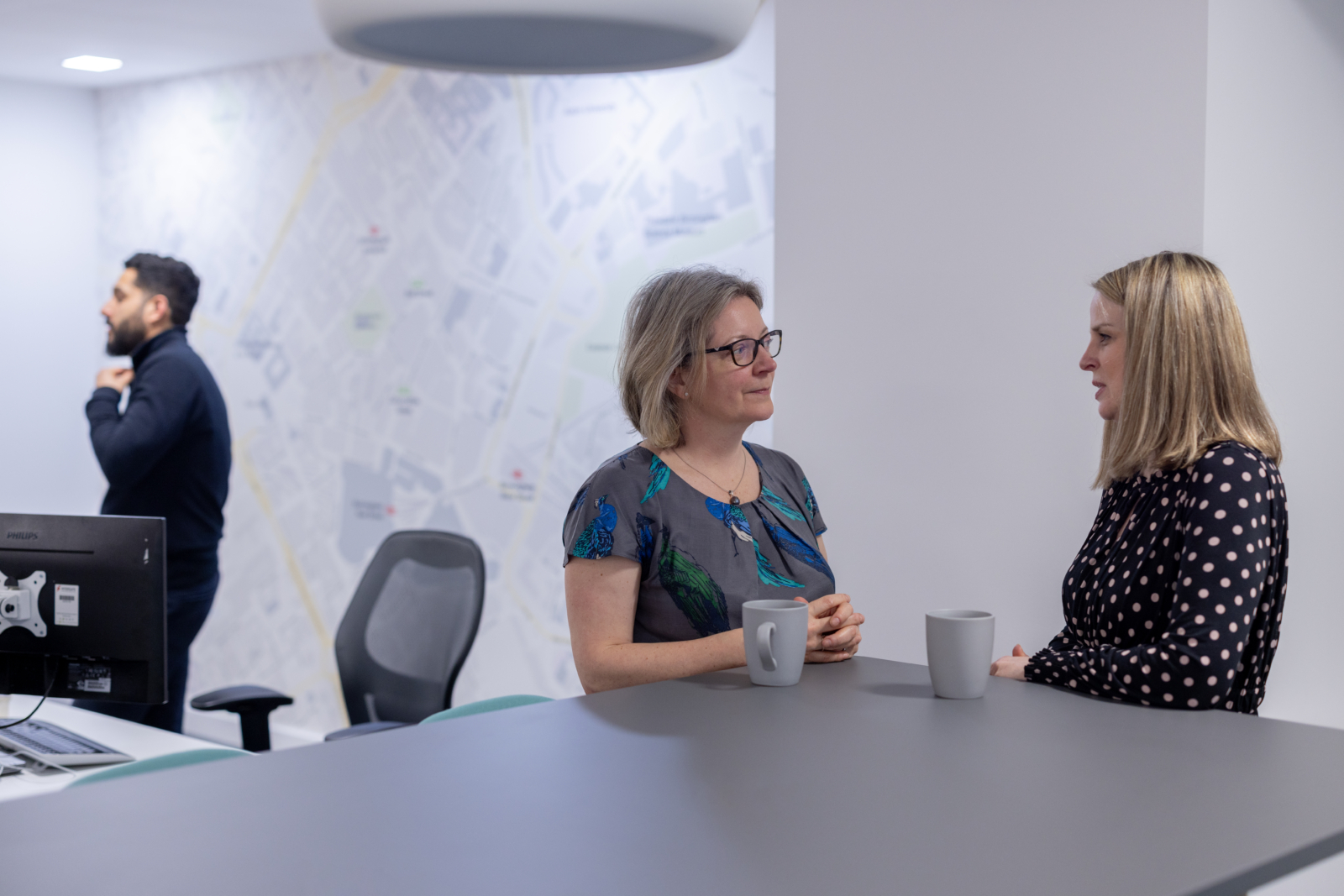 two solicitors stood at a high table talking with an office desk in the background