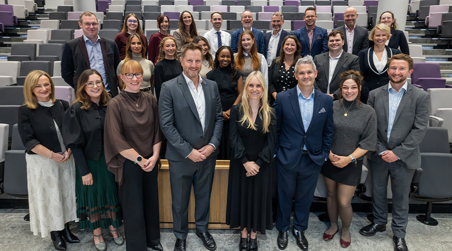 Restructuring and Insolvency team group photo in a modern lecture theatre, with around 25 people in business attire posed across tiered seating.