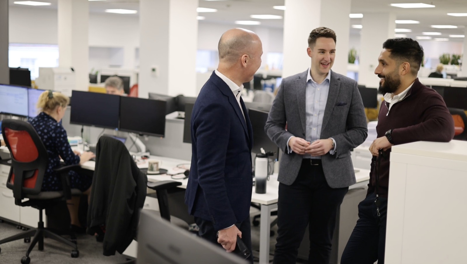 Three of our team standing in the office next to a desk talking