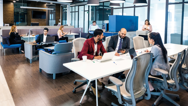 A diverse team of professionals working at desks in a modern office space, collaborating and focusing on their tasks.