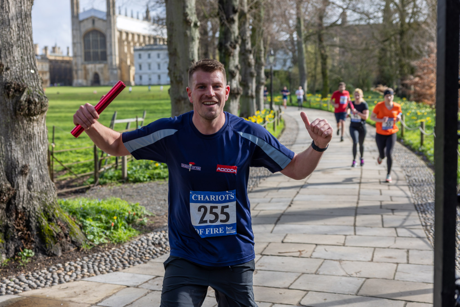 A runner holding a relay baton, giving a thumbs up to the camera