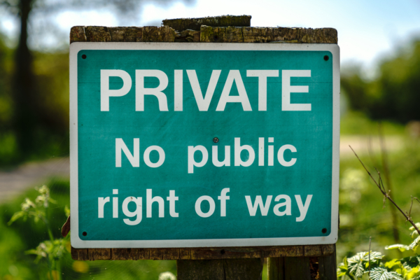 A green sign that is attached to a wooden post with a field in the background. The sign says Private no public right of way
