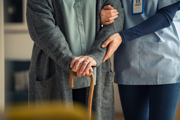 Elderly woman with stick being helped to walk by care worker, from shoulders down