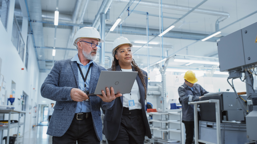 2 people in hard hats walking through workplace with laptop