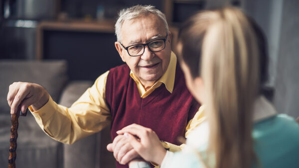 Photo of a man with a cane sitting with his carer