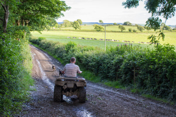 A farmer riding a quadbike with his sheepdog