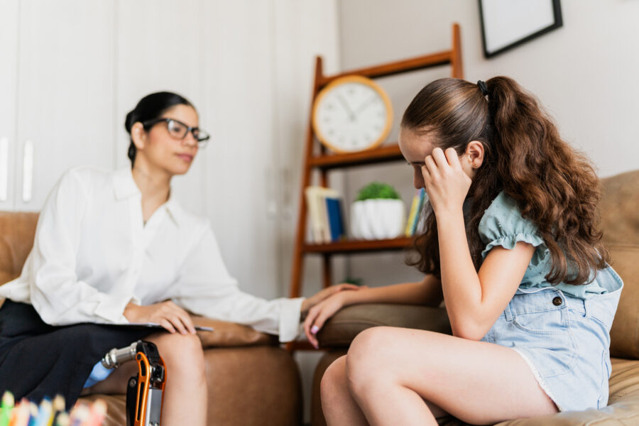 Sad child girl being comforted by psychotherapist during therapy session at clinic