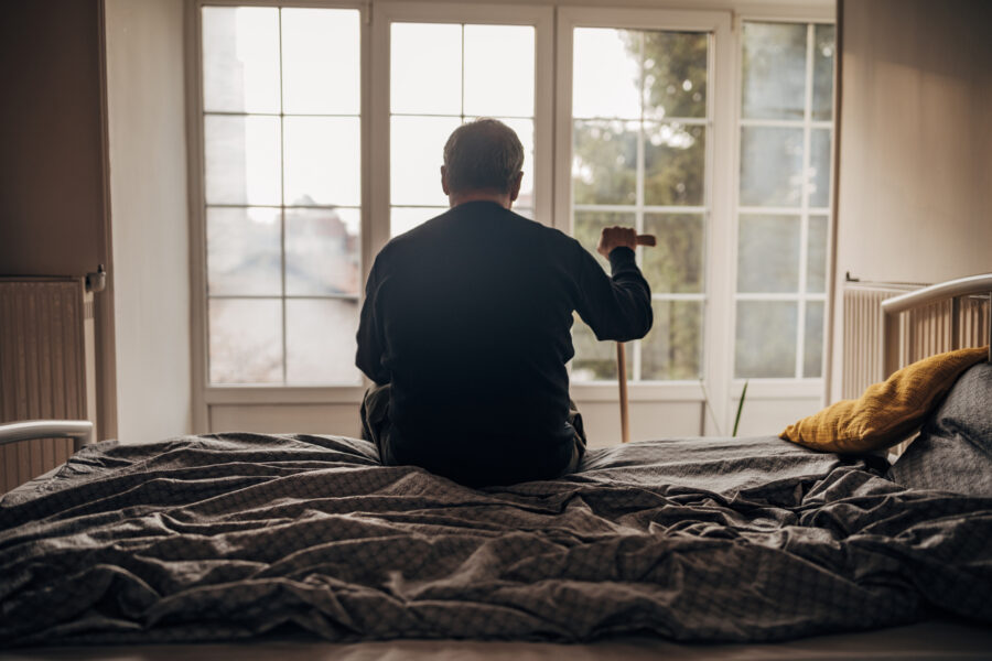 Man is sitting on the bed, looking out the window.