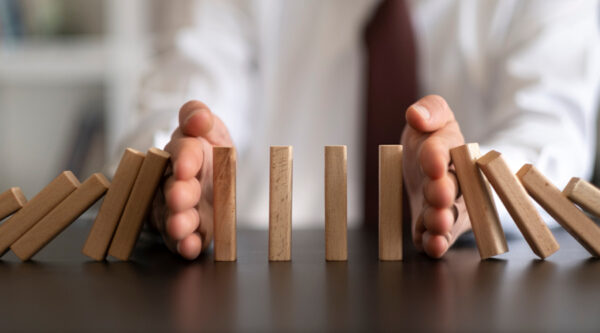 Hands stopping dominoes from falling
