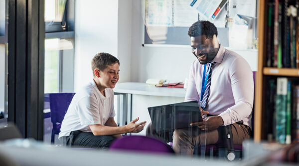 Teacher and pupil in a classroom, looking at a digital tablet