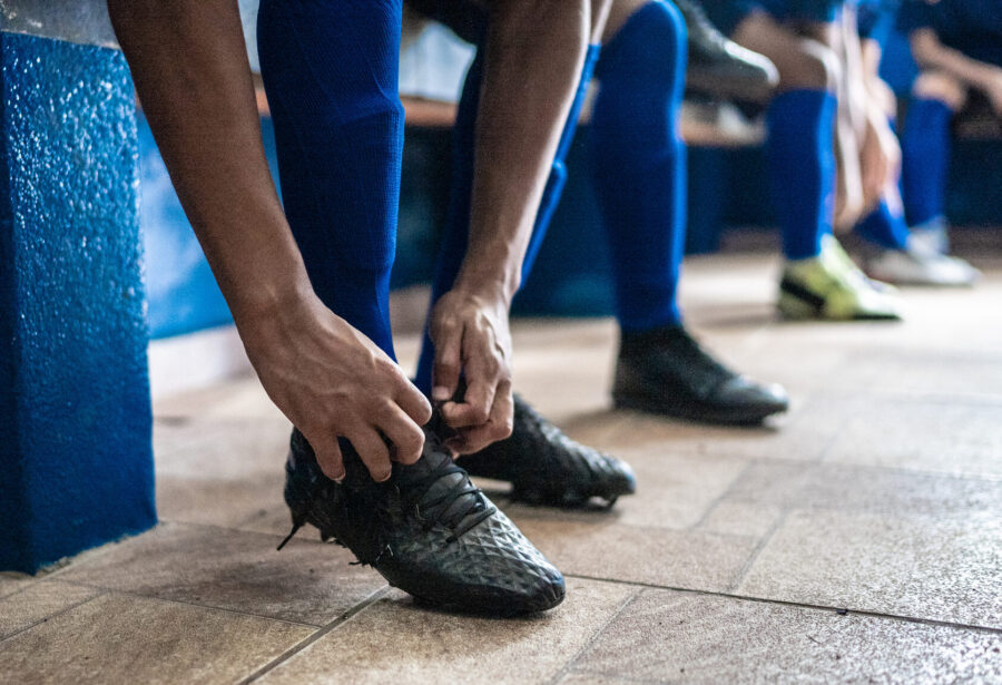 Football player tying shoelaces while preparing for match in the locker room