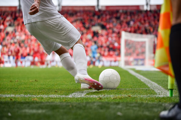 Footballer takes the corner. Detail of player's legs and the ball during football match.