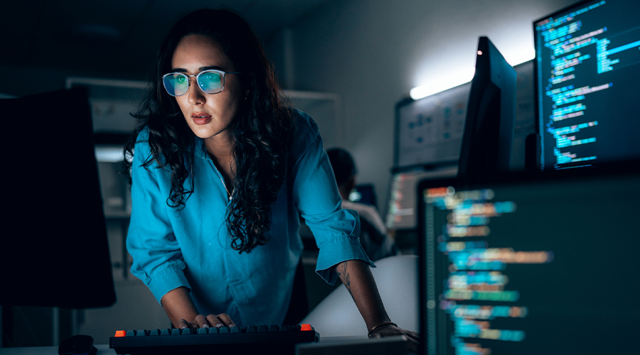 An individual working at a computer in a low‑lit office, with multiple monitors displaying lines of code, suggesting activity related to data processing or information security.