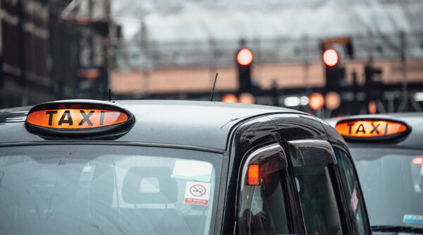 Close-up of London taxis with illuminated ‘taxi’ signs in urban traffic, symbolising transport and emerging driverless vehicle litigation risks.