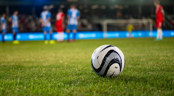 Football resting on grass pitch in foreground with players in the background, representing professional football and employment law issues in sport.