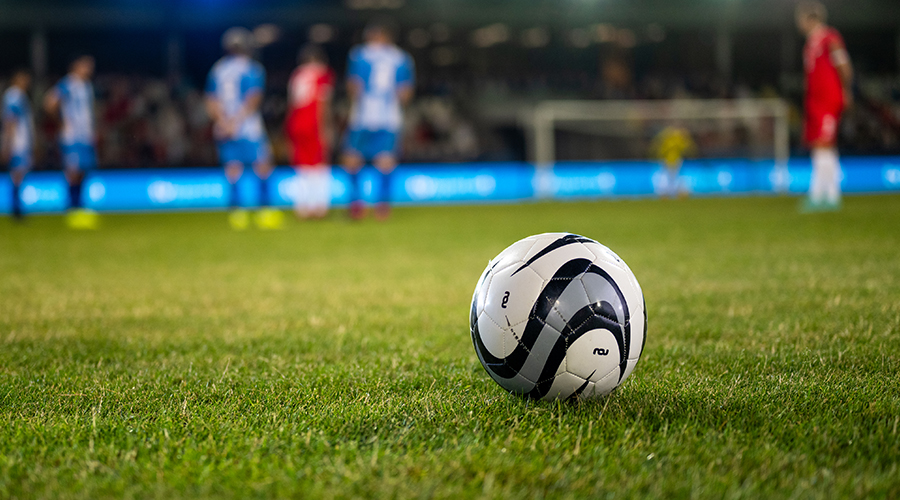 Football resting on grass pitch in foreground with players in the background, representing professional football and employment law issues in sport.