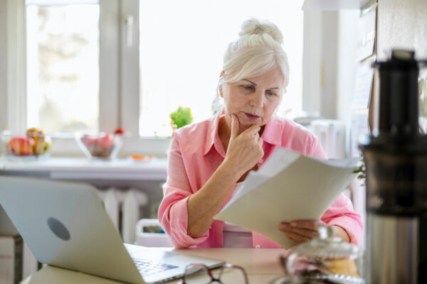 Older woman reviewing paperwork beside a laptop, highlighting the need for professional advice when preparing a will with AI.