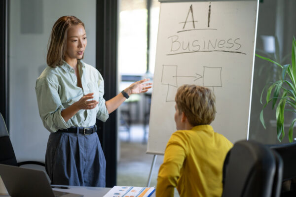 Businesswoman explaining artificial intelligence strategy to colleague, using a whiteboard in a meeting room