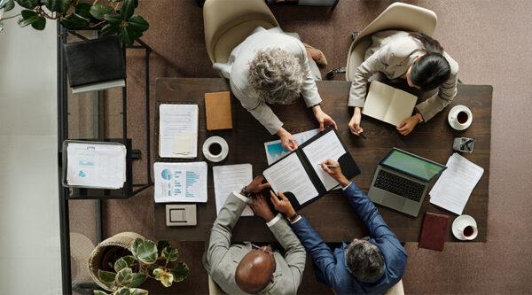 Overhead view of four professionals reviewing commercial contracts and business documents around a table.