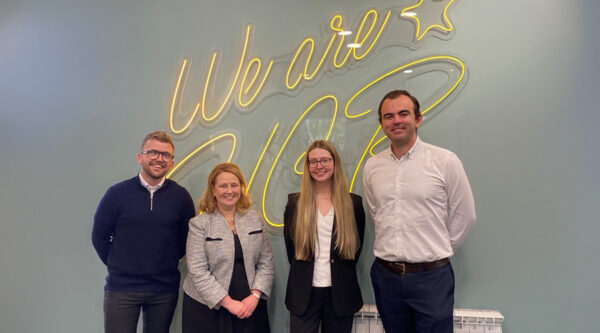 Four members of HCR Law’s Education team stand in front of a “We are HCR” sign following new strategic appointments.