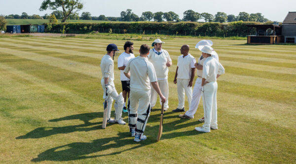 Cricket players and officials discuss tactics on a sunlit cricket pitch.