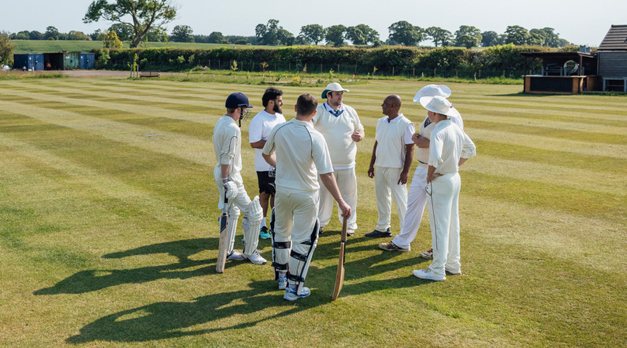 Cricket players and officials discuss tactics on a sunlit cricket pitch.