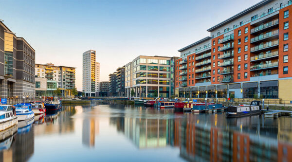 Modern marina waterfront with moored boats, apartments and commercial buildings reflected in calm water.