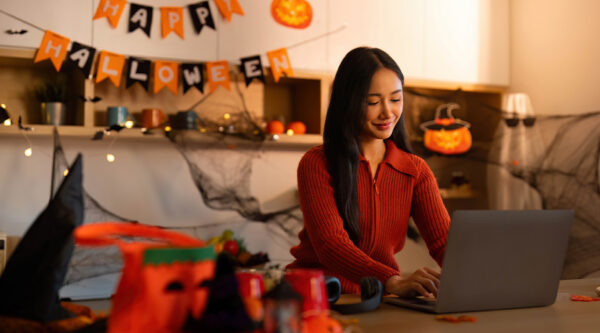 Halloween-themed home workspace with a person using a laptop, surrounded by pumpkin decorations, cobwebs and festive bunting.