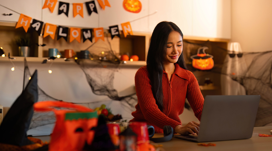 Halloween-themed home workspace with a person using a laptop, surrounded by pumpkin decorations, cobwebs and festive bunting.