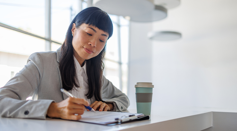 Person writing on a clipboard at a desk, illustrating workplace planning and menopause policy review.