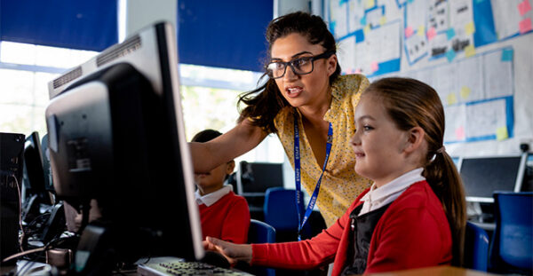 A teacher working in a classroom with a pupil at a computer