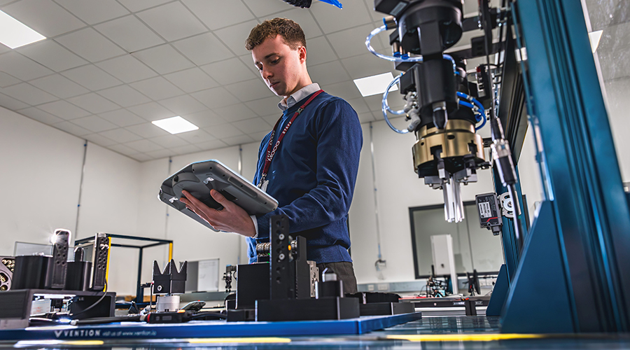 Engineer operating automated manufacturing equipment with a handheld control panel in a technology lab.