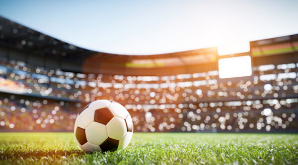 Football on the pitch inside a sunlit stadium.