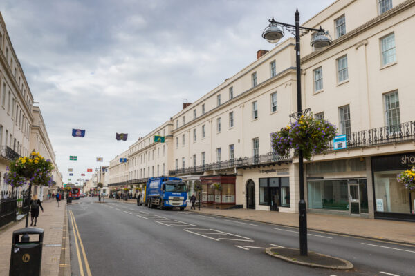 Leamington Spa street lined with elegant cream-coloured Georgian buildings, hanging flower baskets and flags suspended above the road.
